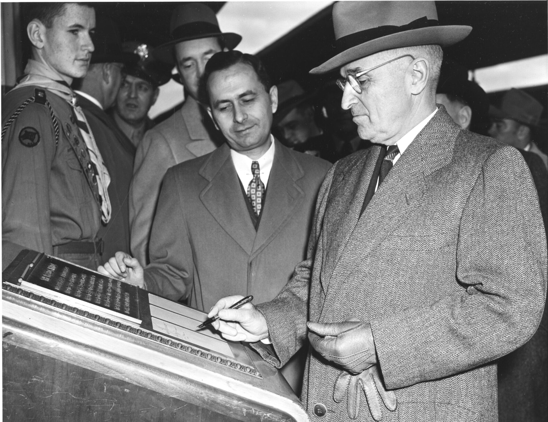 Black-and-white archival photo: an official signs at a desk while a crowd watches, a decision everyone in the room will have to live with, like a Fed rate hike that sets the price of every new corporate bond.