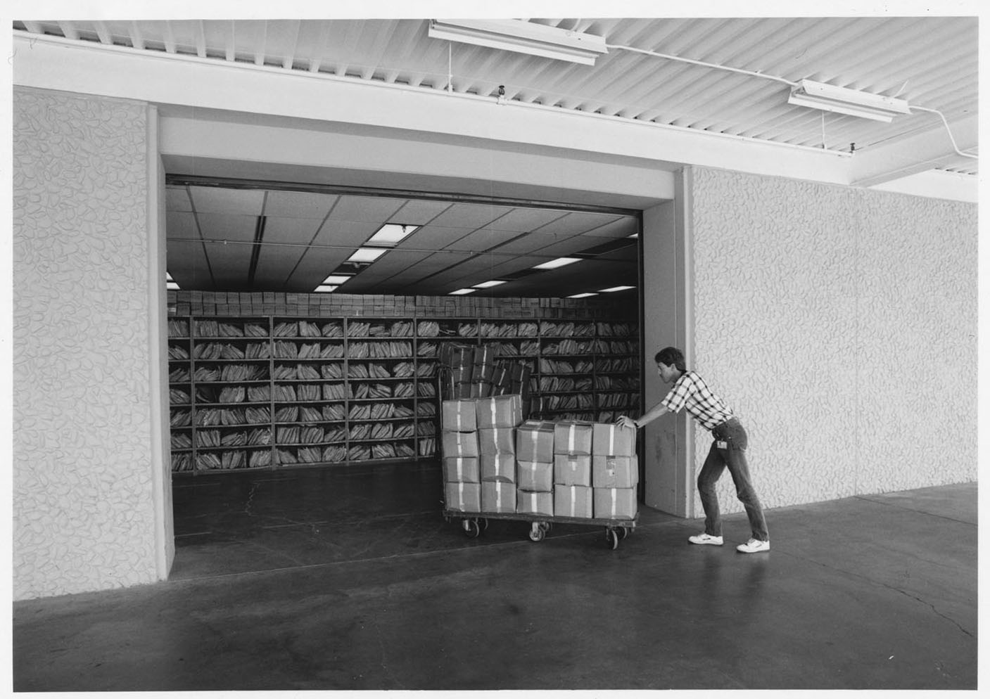 photograph-of-service-branch-chief-roy-garrett-supervising-operations-on-the-back-dock_35183692060_o Black-and-white archival photo: a worker wheels boxes into a vast storage room already lined with shelves, like Oracle filling data center space it has committed to lease for up to 19 years.